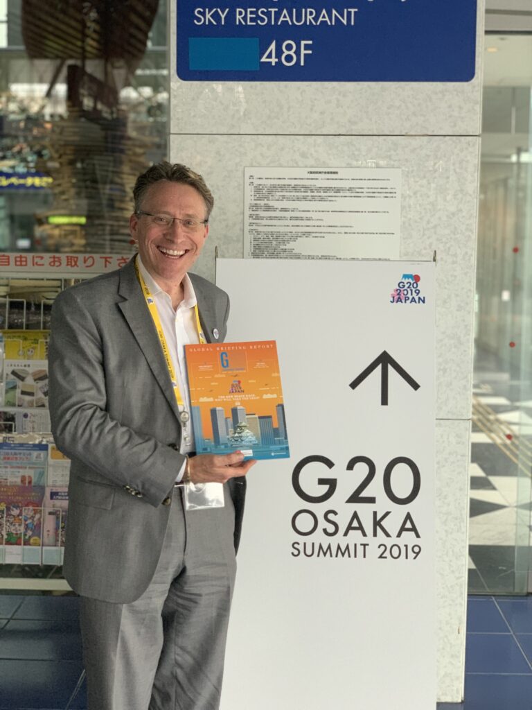 Holding the Group of Nations G20 Japan publication beside the G20 Osaka Summit 2019 sign